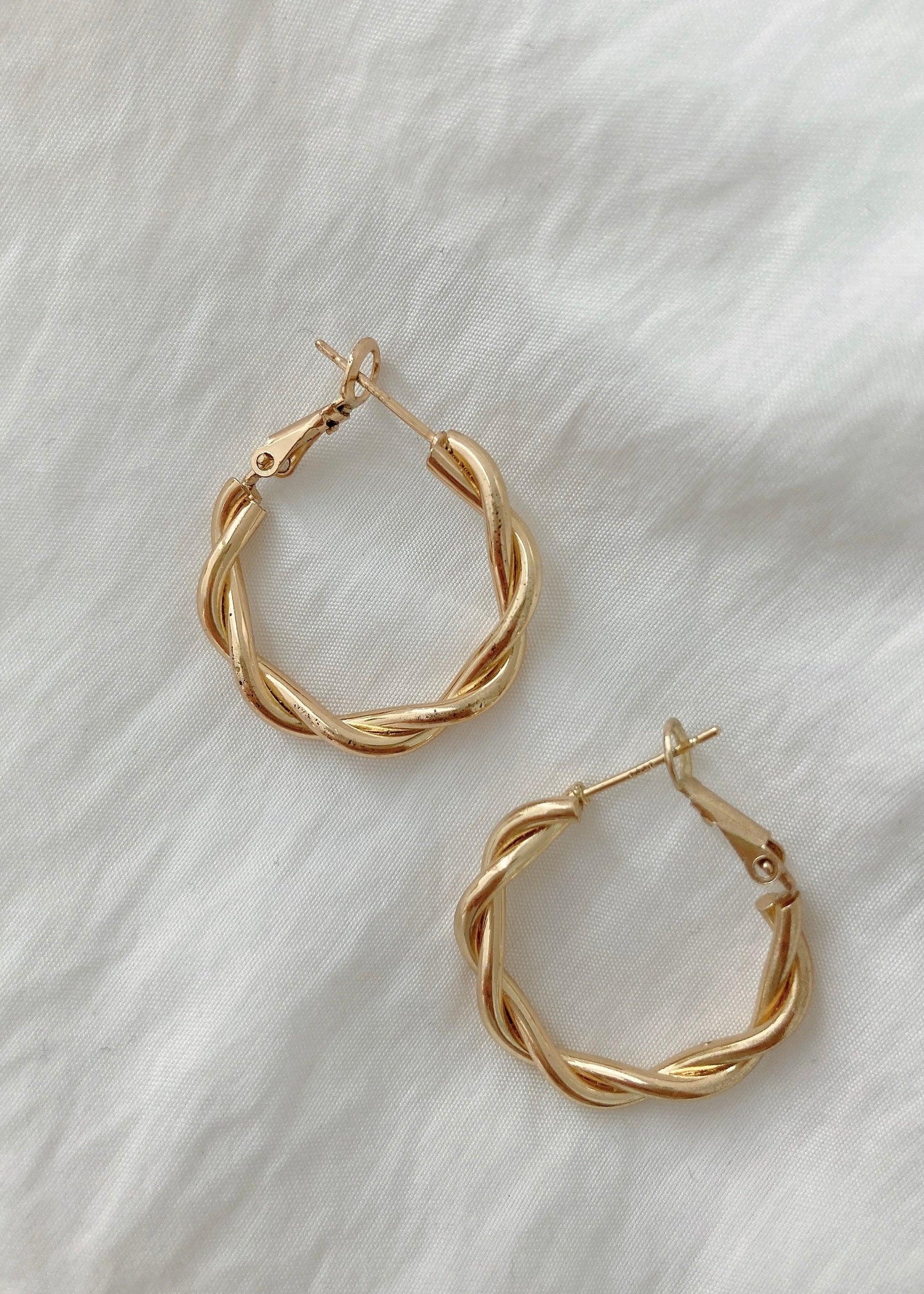 Twisted hoop earrings in 18K gold plated 925 silver with a braided design on white fabric